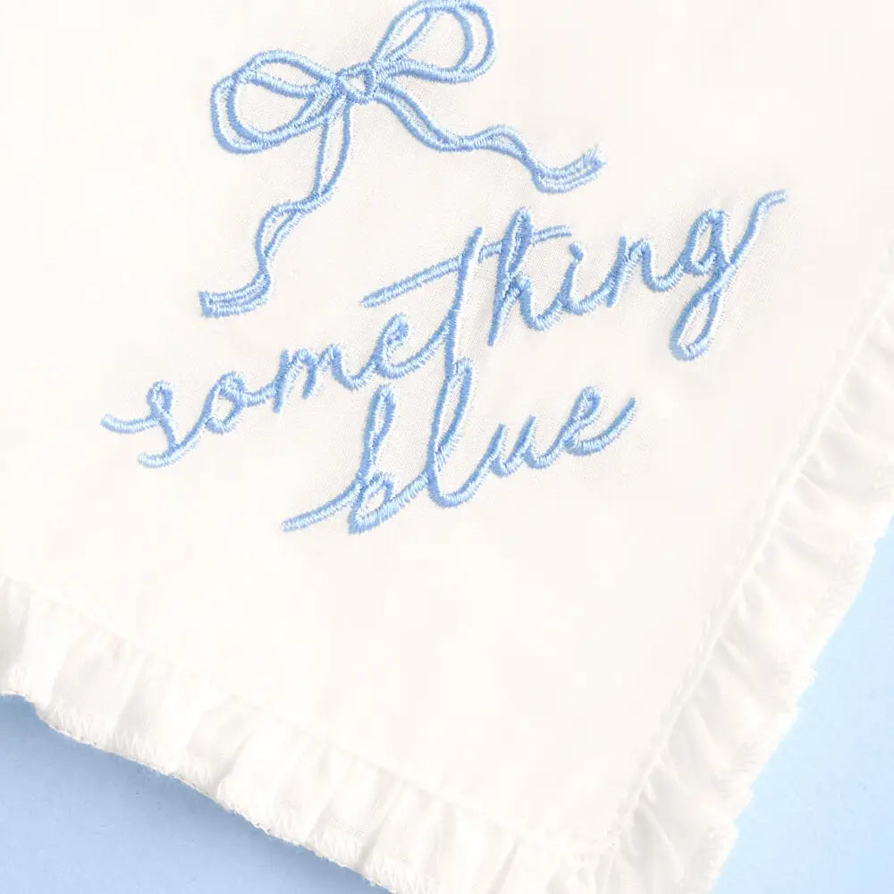 Embroidered text 'Something Blue' on a white fabric background with a blue bow.