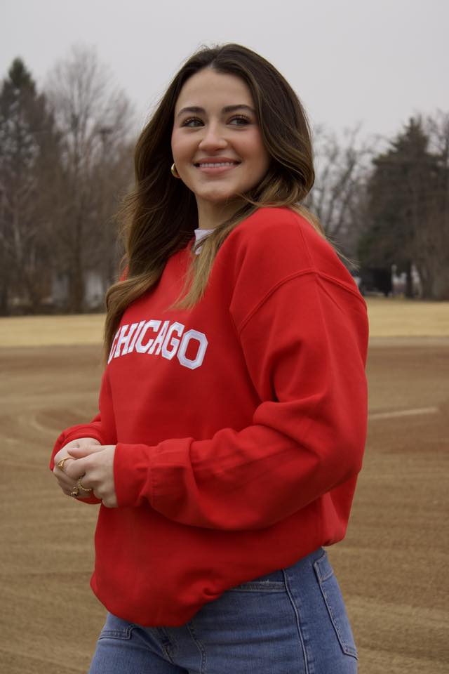Woman wearing a red 'Chicago' sweatshirt standing on a field.