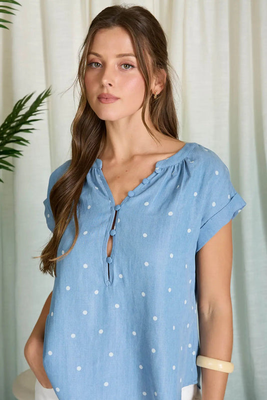 Woman wearing a blue polka dot top against a white curtain background