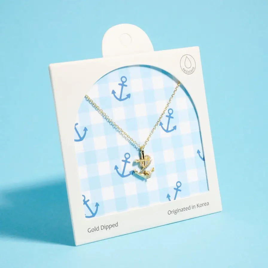 Gold dipped anchor necklace on a branded card with blue background