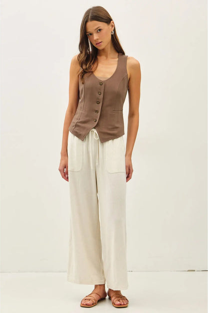Woman wearing a brown sleeveless top and white pants on a white background