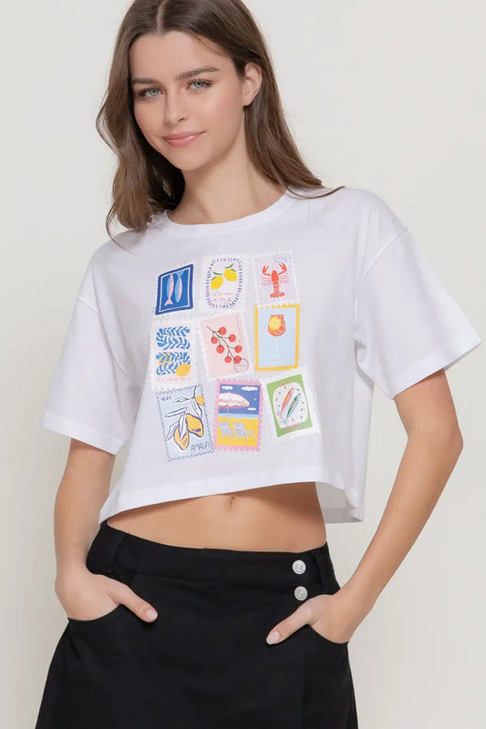 Woman wearing a white crop top with colorful graphic designs on a plain background