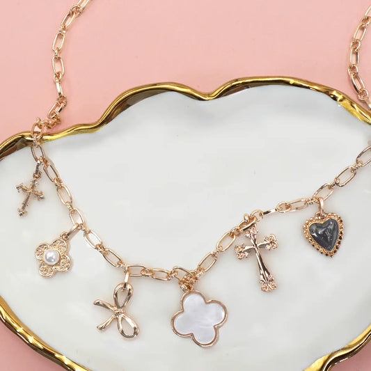 Gold charm bracelet with various charms on a white dish with a pink background