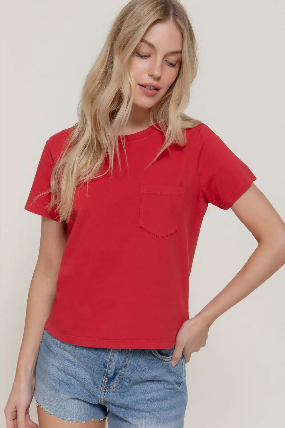 Woman wearing a red t-shirt with a pocket and denim shorts on a plain background