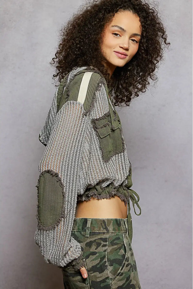 Person wearing a green and gray jacket with camouflage pants against a gray background