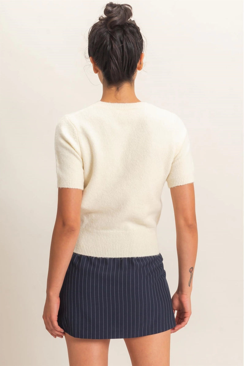A woman shown from the back wearing a cream short-sleeve knit top and a navy blue pinstriped mini skirt, set against a plain light beige background.