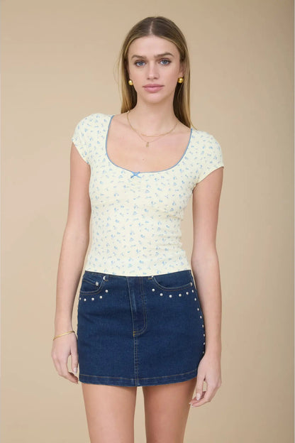 Woman wearing a patterned top and denim skirt against a beige background