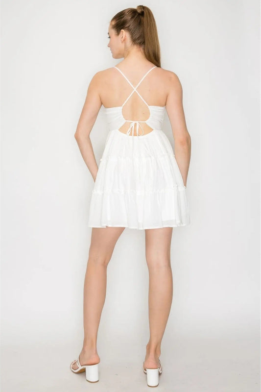Woman wearing a white dress with thin straps and a cutout back on a plain background