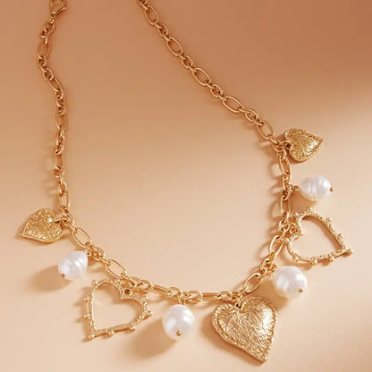 Gold necklace with heart and pearl charms on a beige background