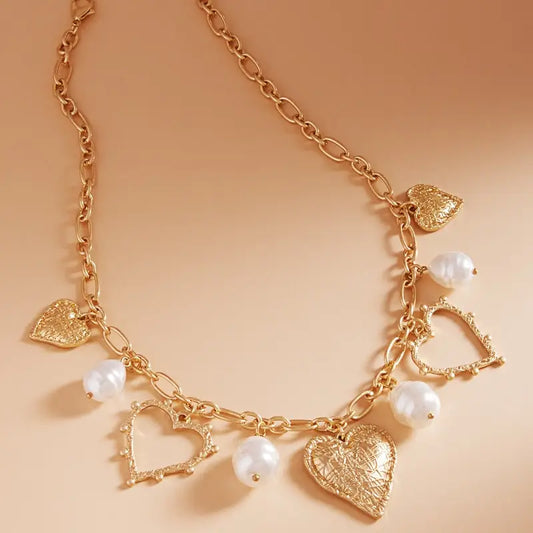 Gold necklace with heart and pearl charms on a beige background