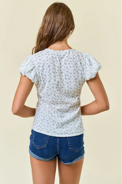 Woman wearing a floral top and denim shorts on a beige background