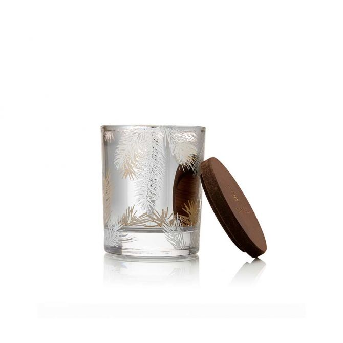 A clear glass candle jar with etched silver pine branches, shown next to its dark brown wooden lid on a white background.