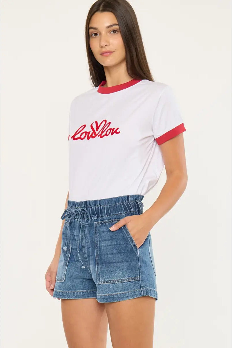 Woman wearing a white t-shirt with red accents and denim shorts on a white background