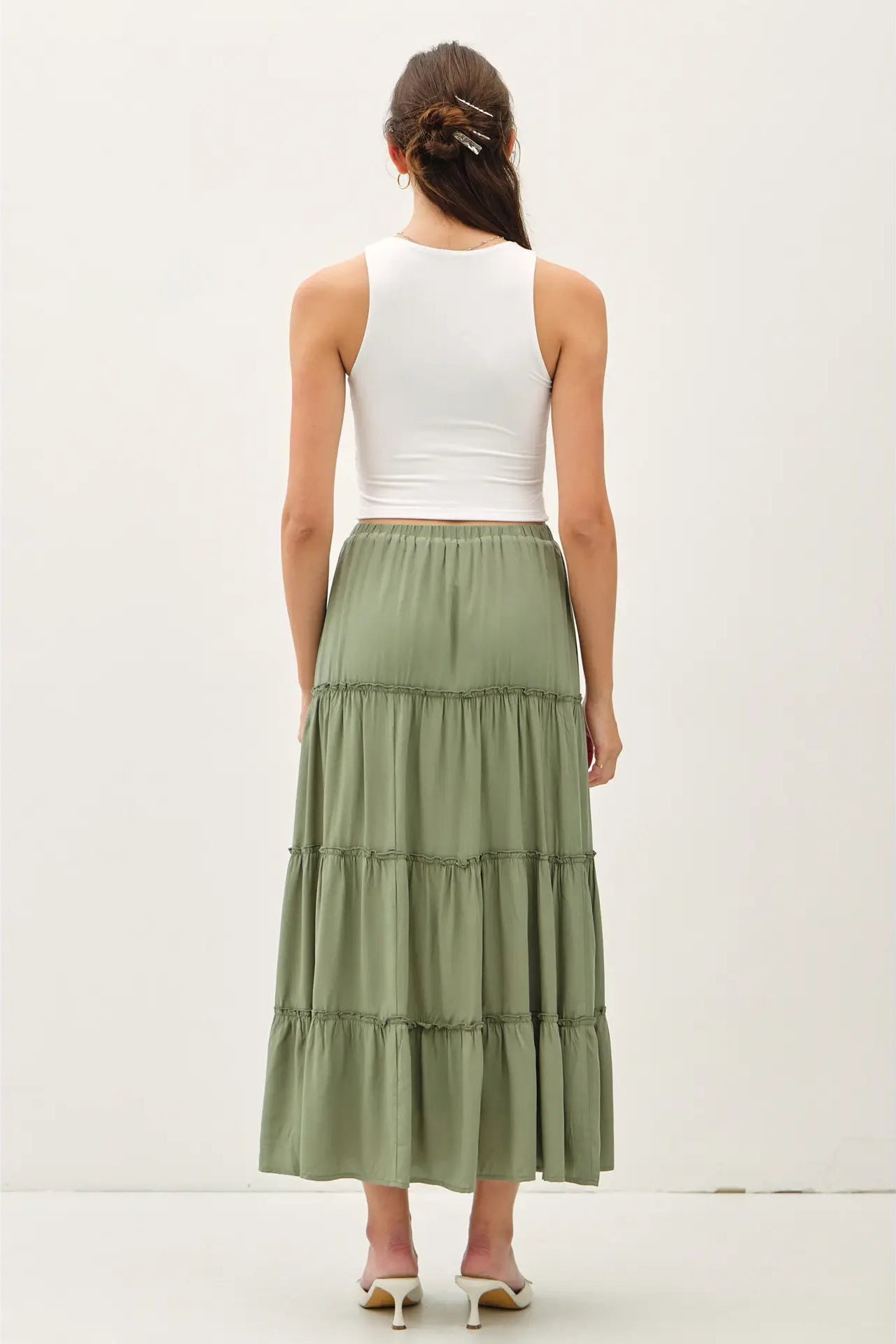 Woman wearing a white top and green tiered skirt on a plain background