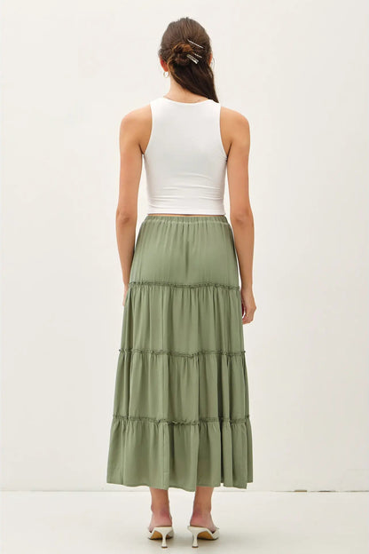 Woman wearing a white top and green tiered skirt on a plain background