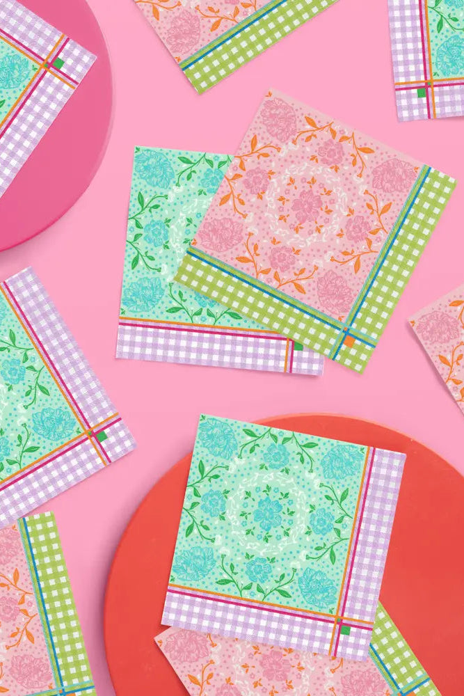A styled flat-lay of multiple decorative paper napkins with colorful patterns, arranged on a pink background with two round plates.