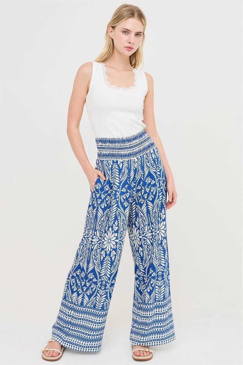 Woman wearing a white sleeveless top and blue patterned pants on a white background