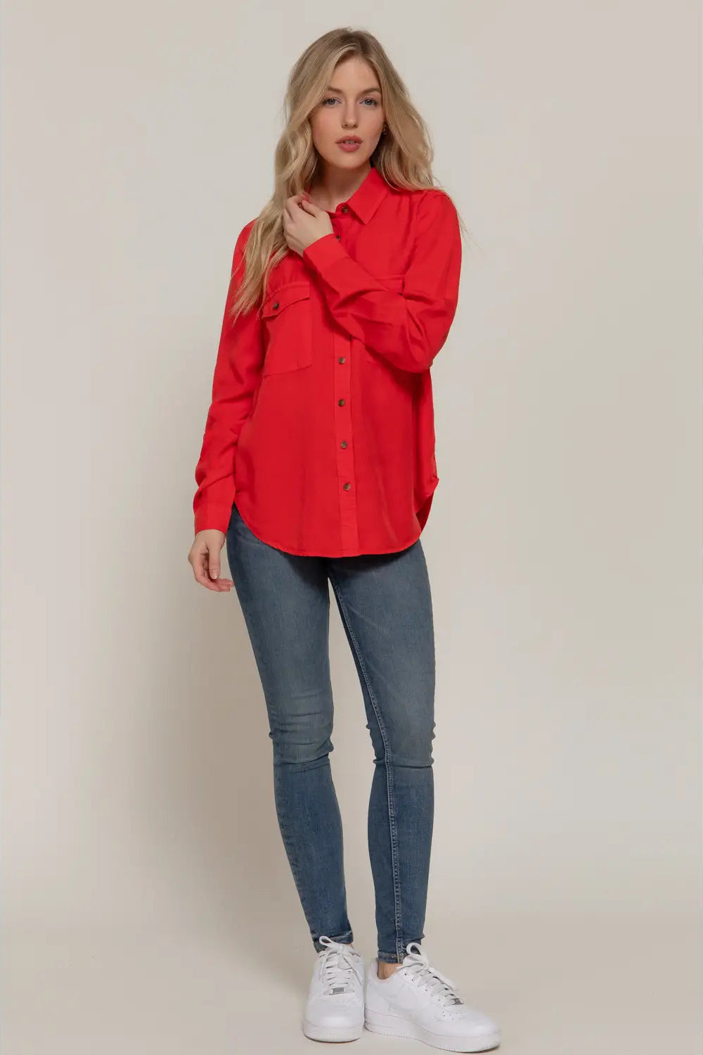 Woman wearing a red shirt and blue jeans against a beige background