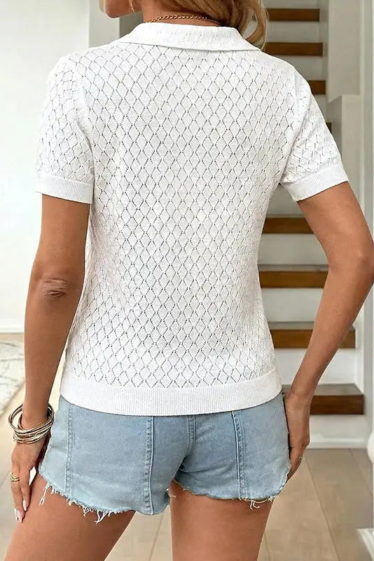 Person wearing a white patterned shirt and denim shorts in a home setting.