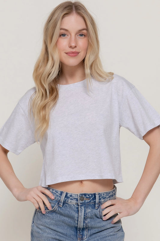 Woman wearing a white crop top and blue jeans against a plain background