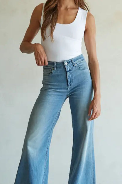 Person wearing a white tank top and blue flared jeans on a plain background