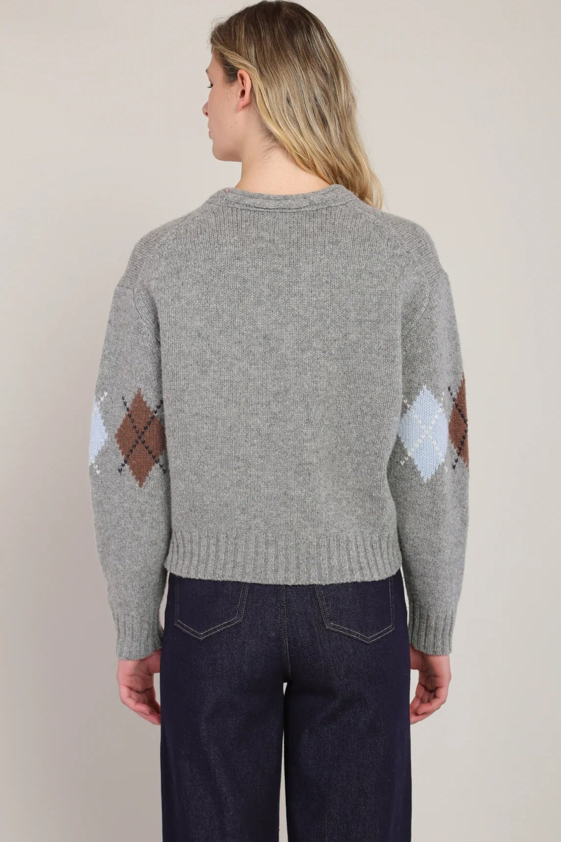 Person wearing a gray sweater with diamond pattern on sleeves against a plain background