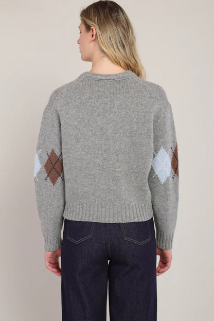 Person wearing a gray sweater with diamond pattern on sleeves against a plain background