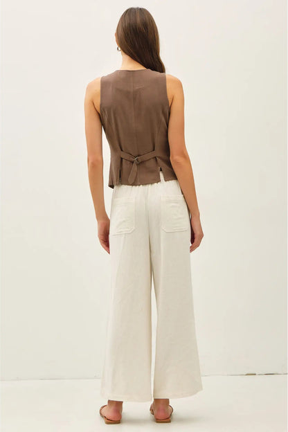 Woman wearing a brown sleeveless top and white pants on a plain background