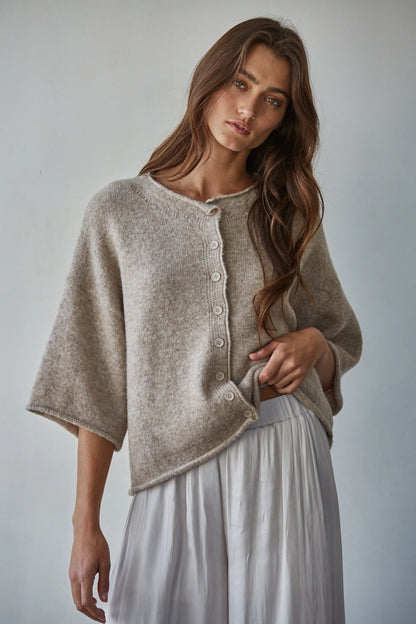 Woman wearing a beige cardigan over a white dress against a plain background
