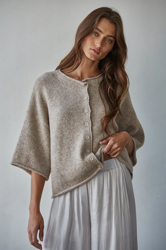 Woman wearing a beige cardigan over a white dress against a plain background