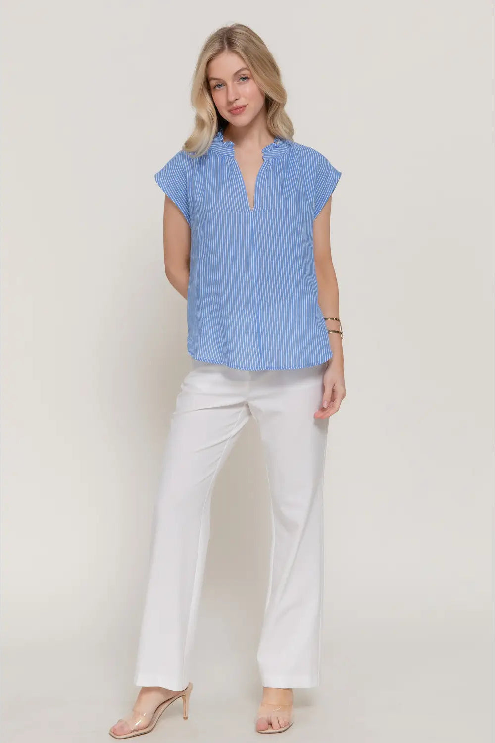 Woman wearing a blue striped shirt and white pants on a plain background