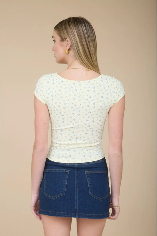 Woman wearing a white floral top and blue denim skirt on a beige background