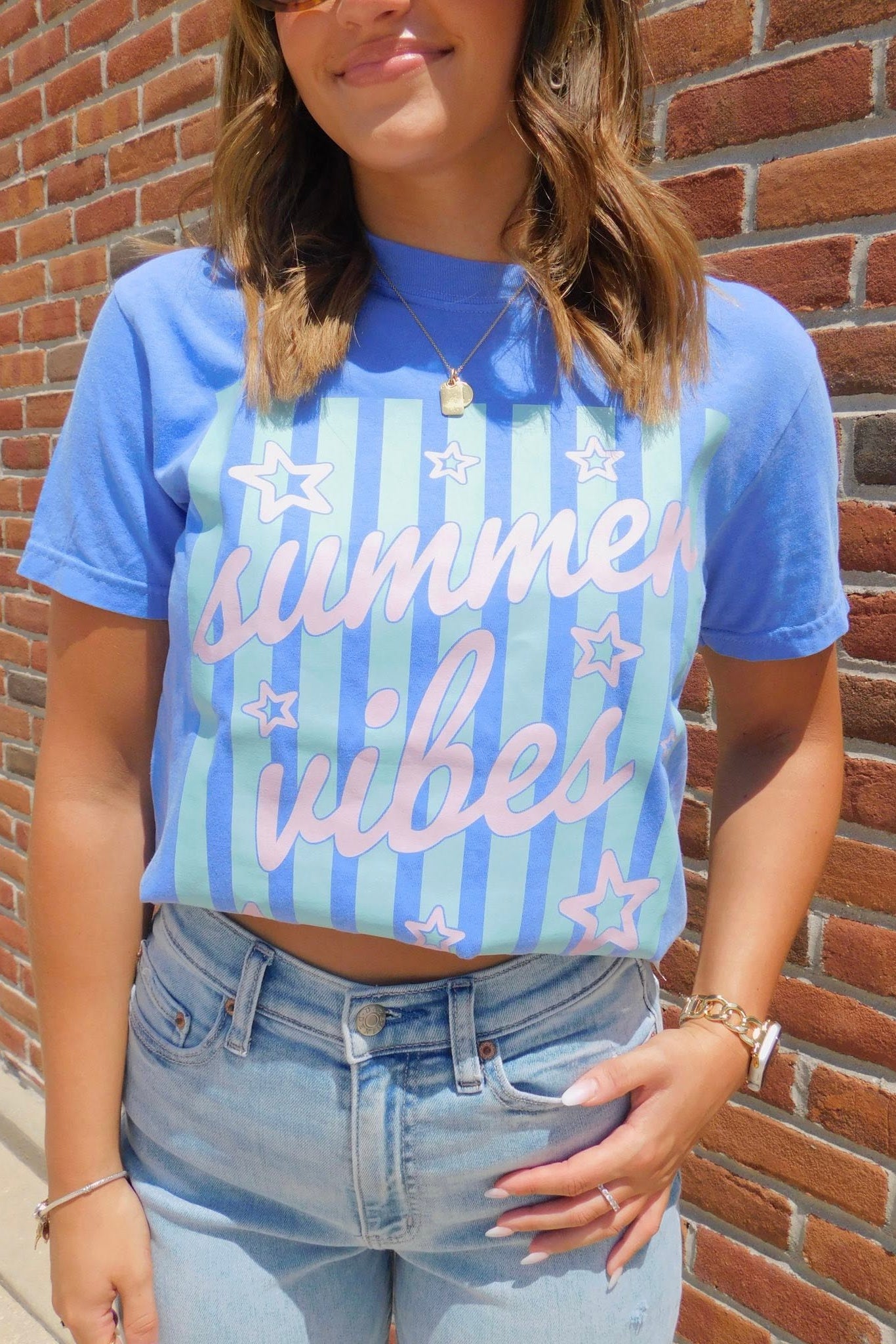 Person wearing a blue 'summer vibes' t-shirt against a brick wall.