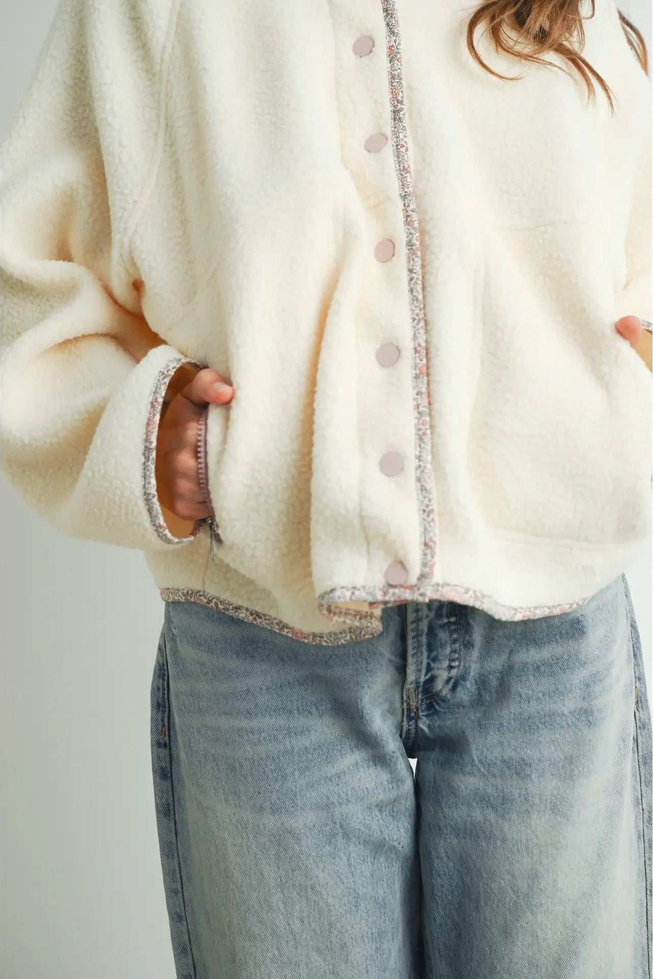 A close-up of a person wearing a cream-colored fuzzy cardigan with pink buttons and light gray denim jeans.