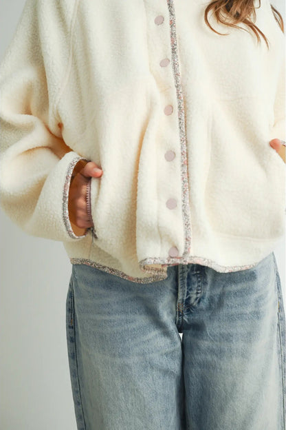 A close-up of a person wearing a cream-colored fuzzy cardigan with pink buttons and light gray denim jeans.