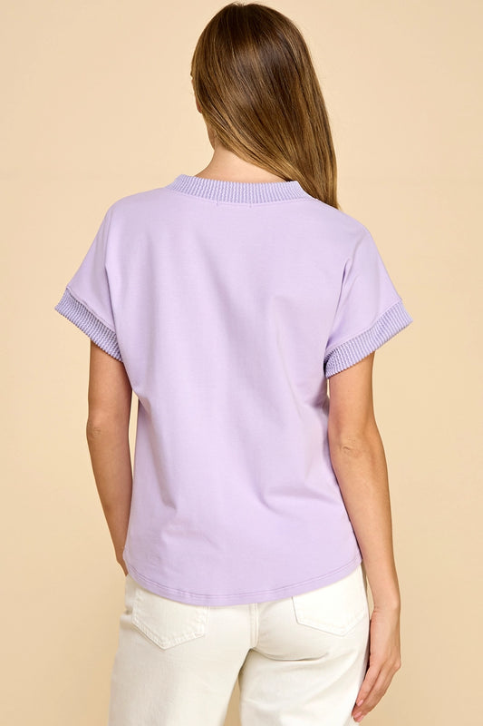 Person wearing a light purple sweater with short sleeves on a beige background