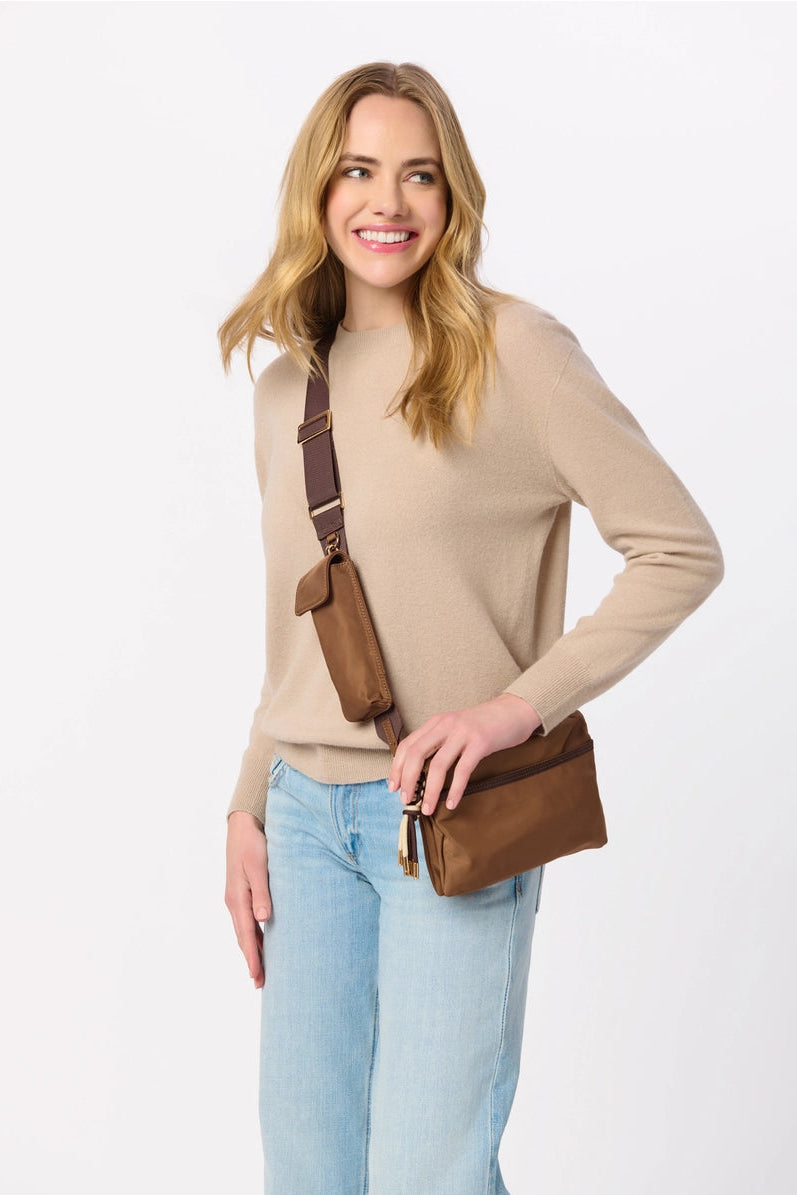 Woman wearing a beige sweater and light blue jeans with a brown leather bag on a white background
