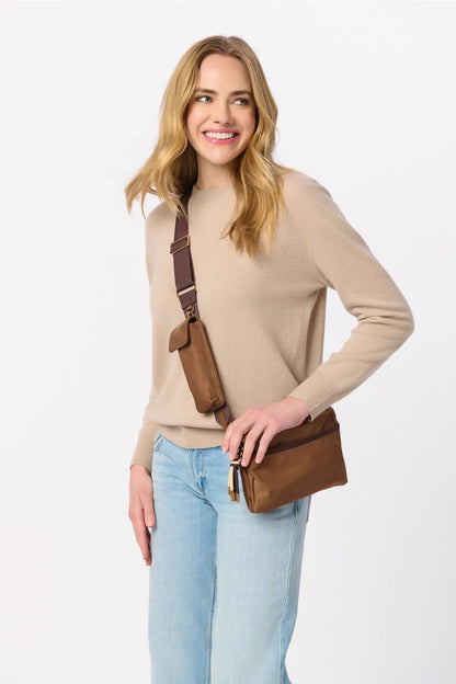 Woman wearing a beige sweater and light blue jeans with a brown leather bag on a white background