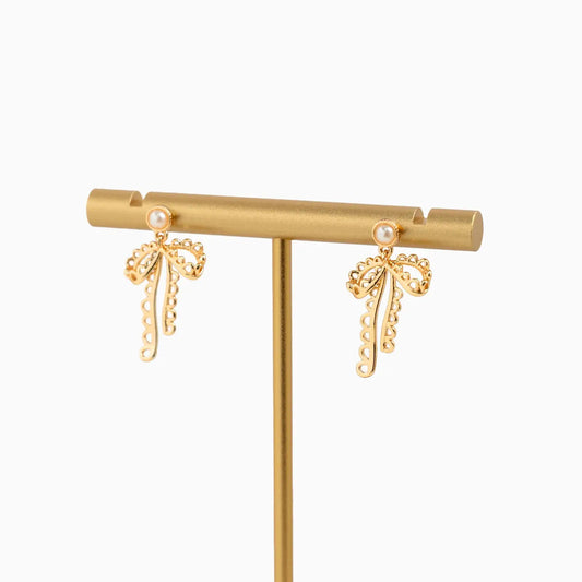 Gold bow-shaped earrings on a gold earring stand against a white background
