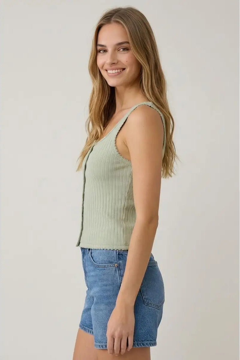 Woman wearing a green ribbed tank top and denim shorts on a plain background