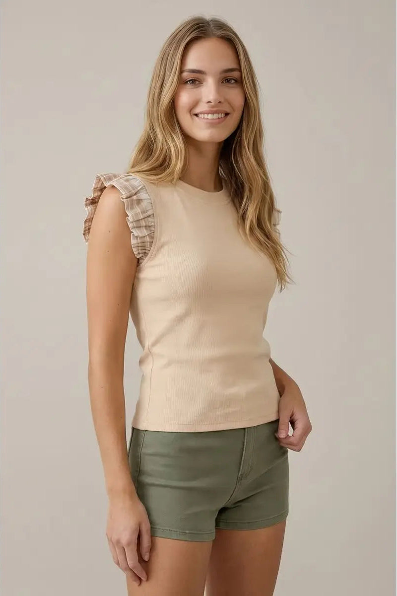 Woman wearing a beige sleeveless top and green shorts against a plain background