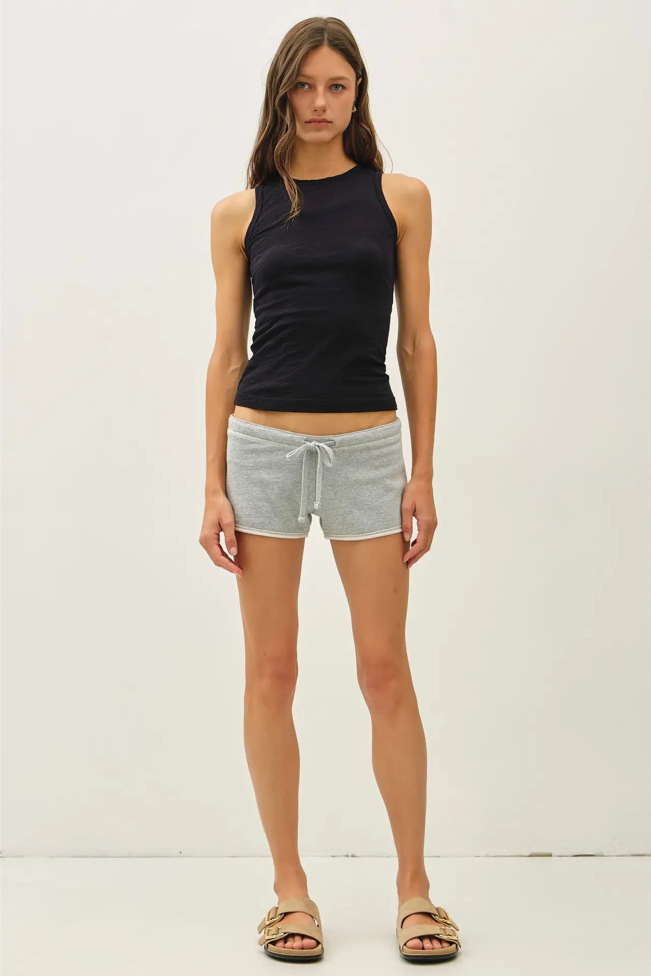 A woman modeling a sleeveless black ribbed tank top and light gray heathered drawstring shorts against a plain off-white studio background.