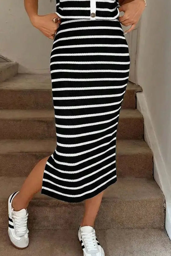 A woman wearing a sleeveless black and white horizontally striped midi dress with a V-neckline and button details, paired with white sneakers, standing on indoor concrete stairs.