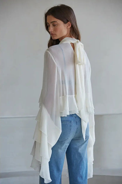 Woman wearing a white layered scarf and blue jeans against a plain background
