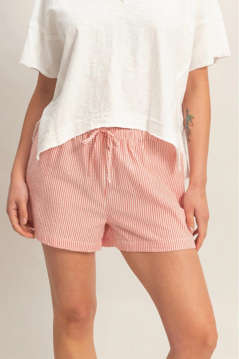 Person wearing a white top and pink striped shorts on a plain background