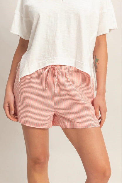 Person wearing a white top and pink striped shorts on a plain background