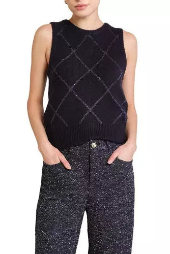 A model wearing a sleeveless black knit sweater vest with a subtle silver argyle pattern, paired with dark speckled trousers, against a plain white background.