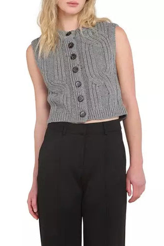 A woman wearing a gray sleeveless cable-knit vest with dark buttons and black trousers, shown from the neck down against a plain white background.