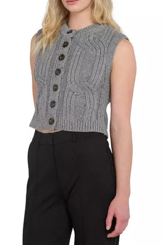 A woman wearing a gray sleeveless cable-knit cropped vest with dark buttons, paired with black trousers, shown against a plain white background.