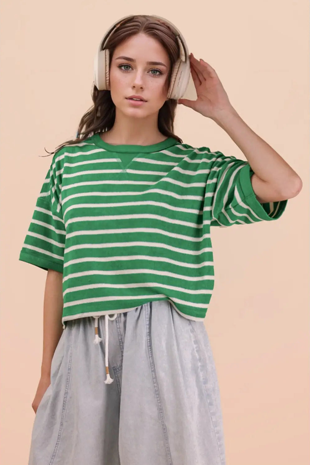 Woman wearing a green and white striped shirt and headphones on a beige background
